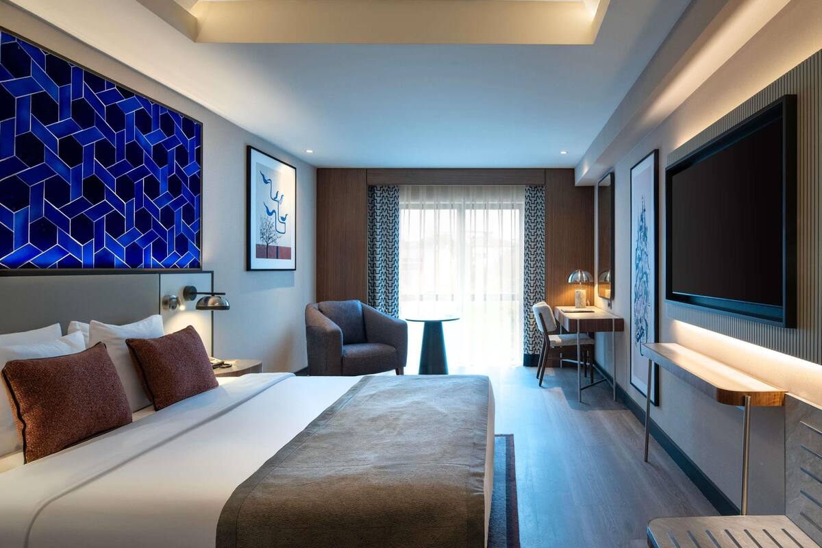 Een moderne hotelkamer met een groot bed, een bureau met stoel, een televisie en een decoratief paneel aan de muur.