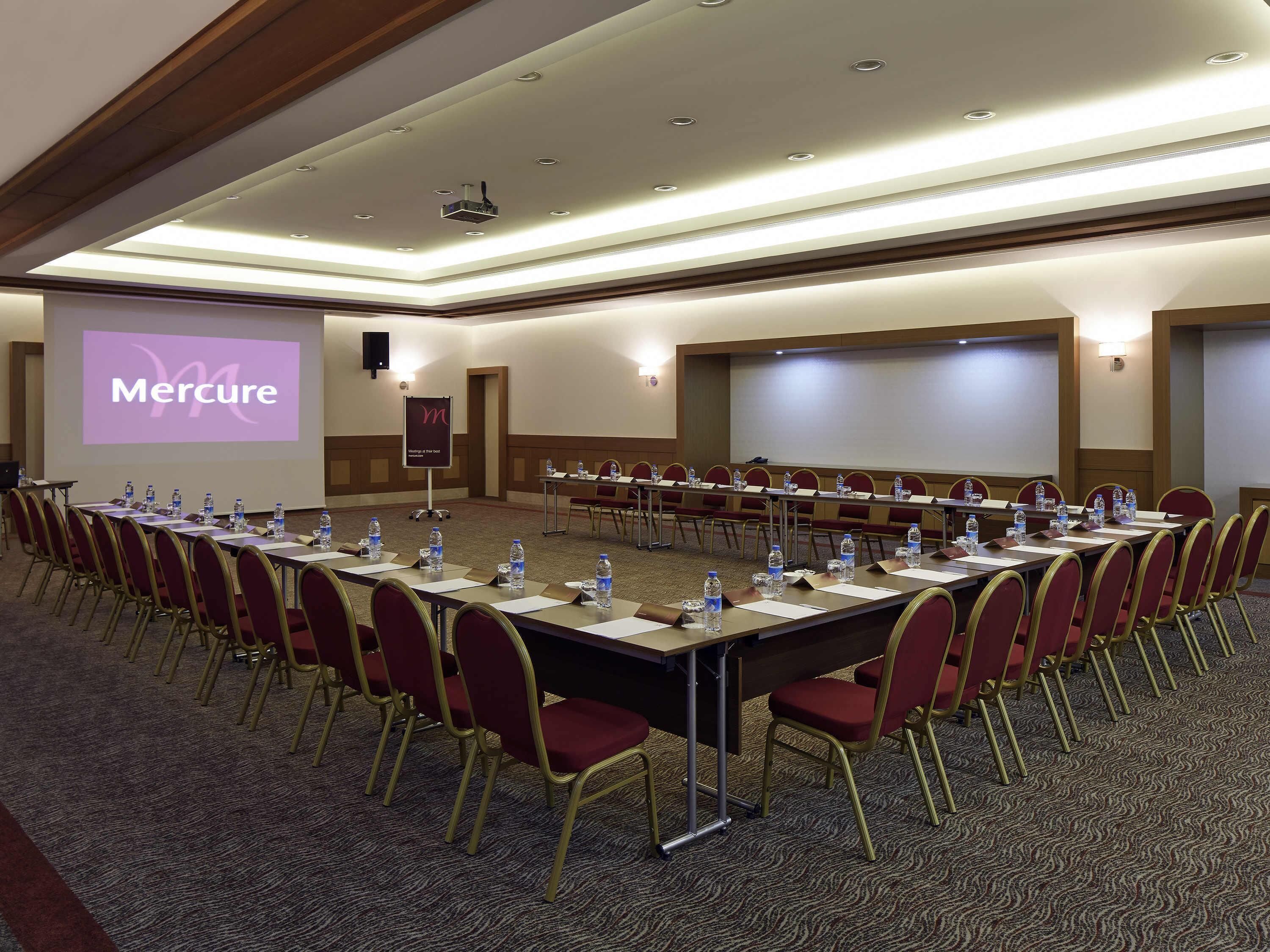 A conference room with a long table, chairs, a projector screen, and a presentation screen.