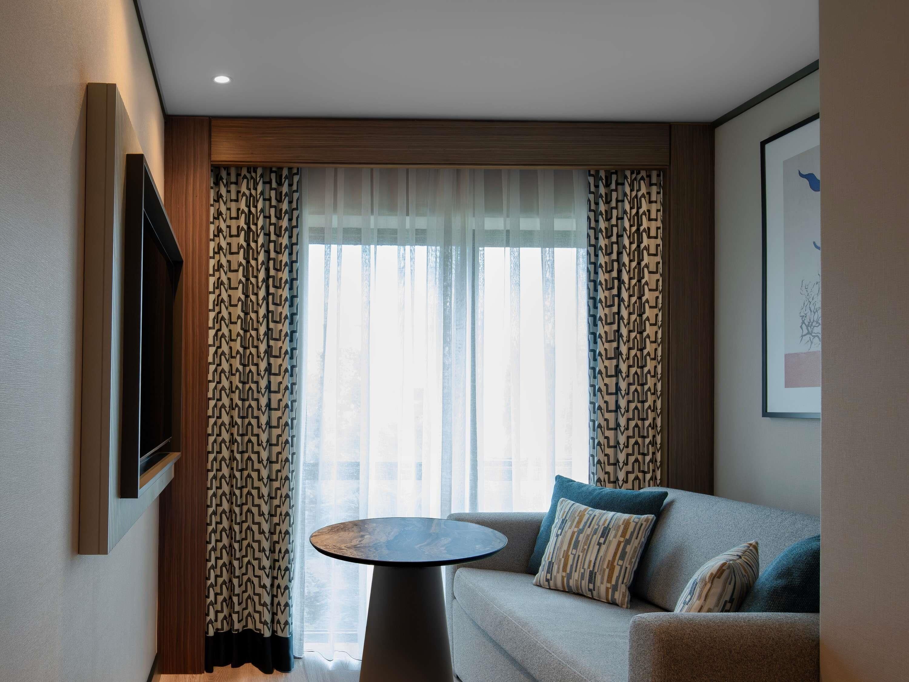 Una habitación de hotel moderna con sofá, una mesa redonda y cortinas estampadas.