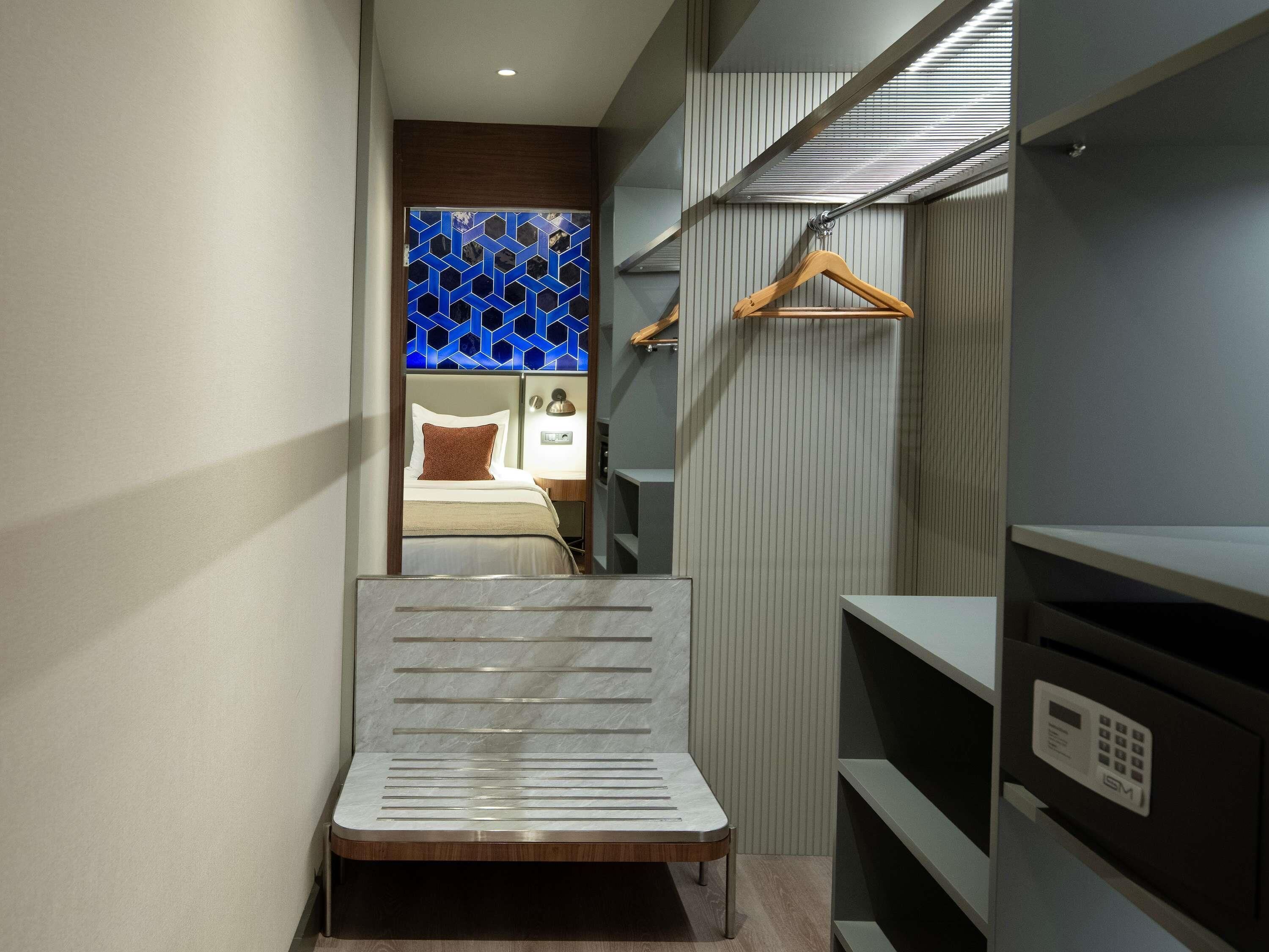 Una habitación de hotel moderna con una cama, un perchero de madera y un armario con espejo.