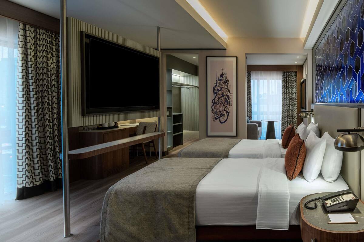 Een moderne hotelkamer met een groot bed, een bureau met een flatscreen televisie, een zithoek met een bank en een groot kunstwerk aan de muur.
