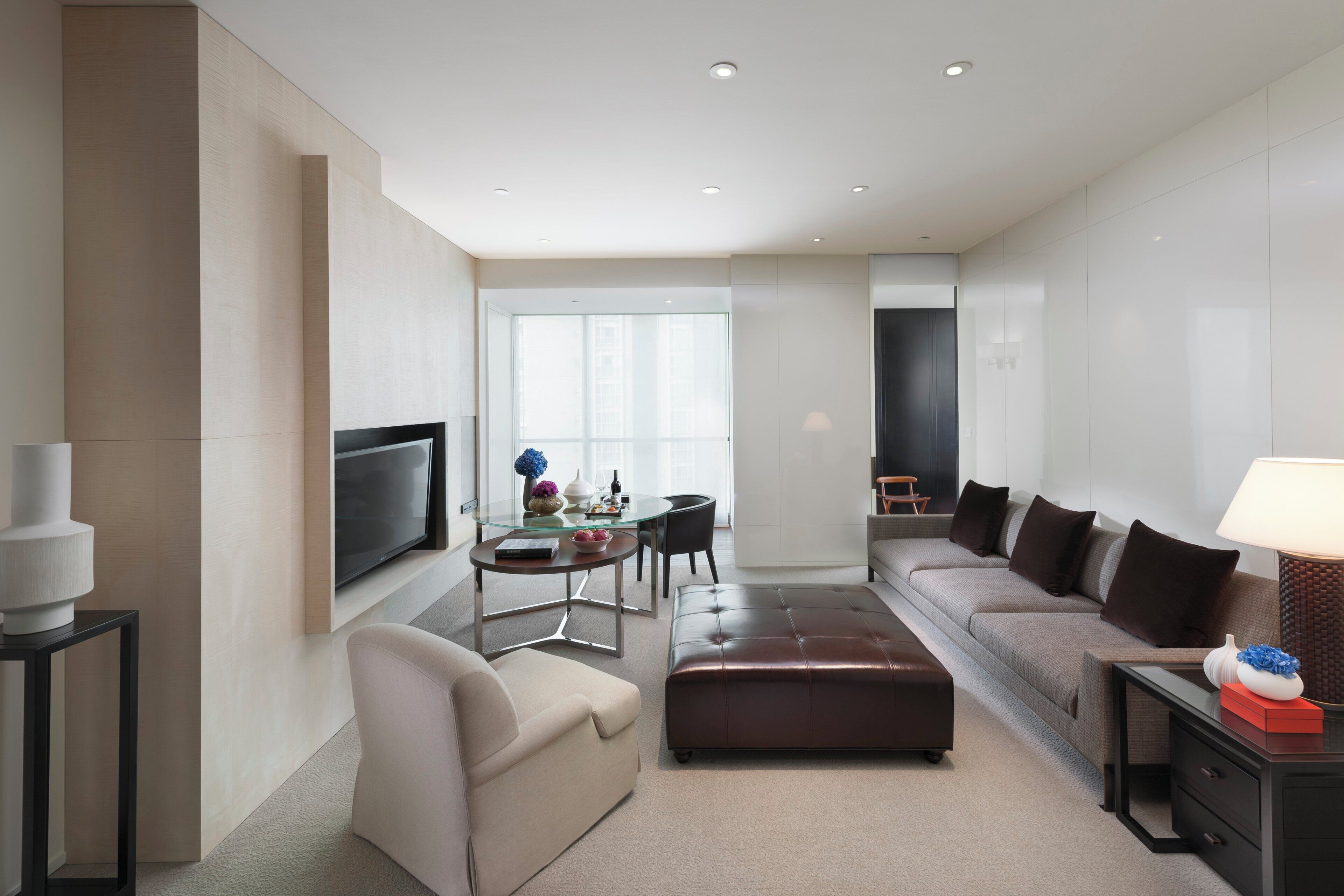 A modern hotel room with a flat-screen TV, a sofa, a dining table, and a large window.