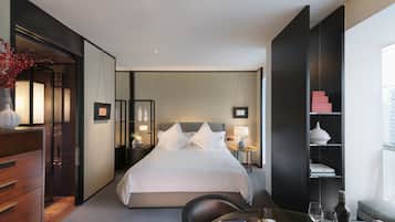 Habitación de hotel con una cama grande, mesitas de noche, un escritorio, una silla, una estantería y una ventana.