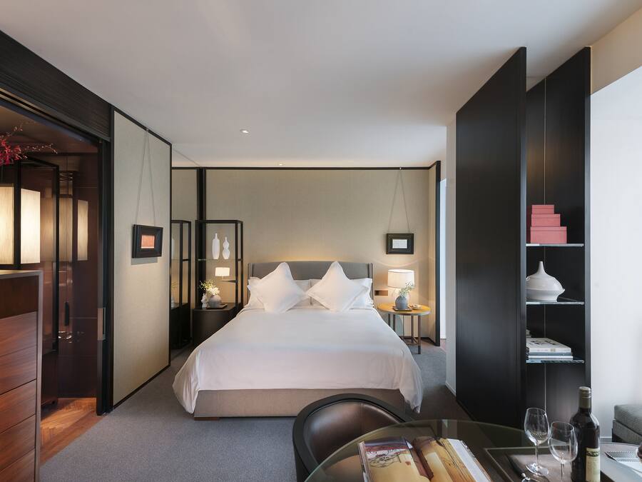 Habitación de hotel con una cama grande, mesitas de noche, un escritorio, una silla, una estantería y una ventana.