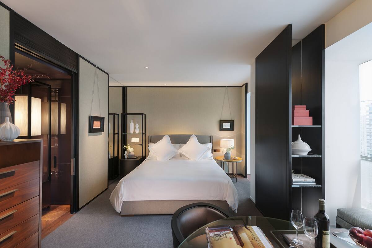 Une chambre d’hôtel moderne dotée d’un grand lit, de tables de chevet, d’un bureau avec une chaise, d’une bibliothèque et offrant une vue sur la ville.