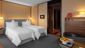 A hotel room with two beds, a desk with a bowl of fruit, and a wooden dresser.