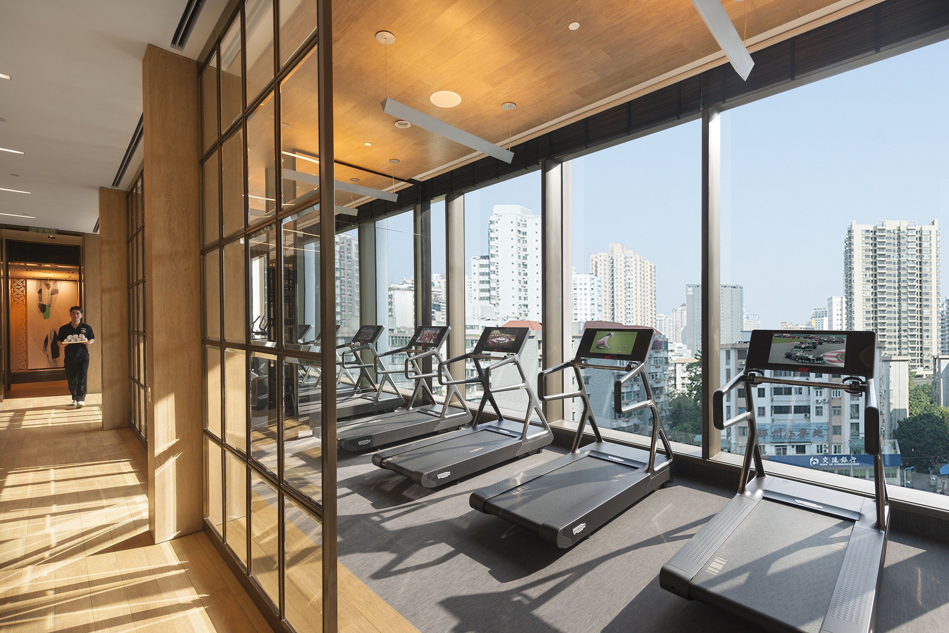 A gym with treadmills and exercise equipment, large windows, and a view of a cityscape.