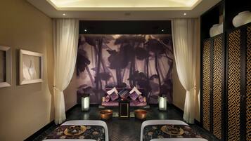 A room with a massage area featuring two massage tables, a wall with a floral mural, and a decorative partition with a geometric pattern.