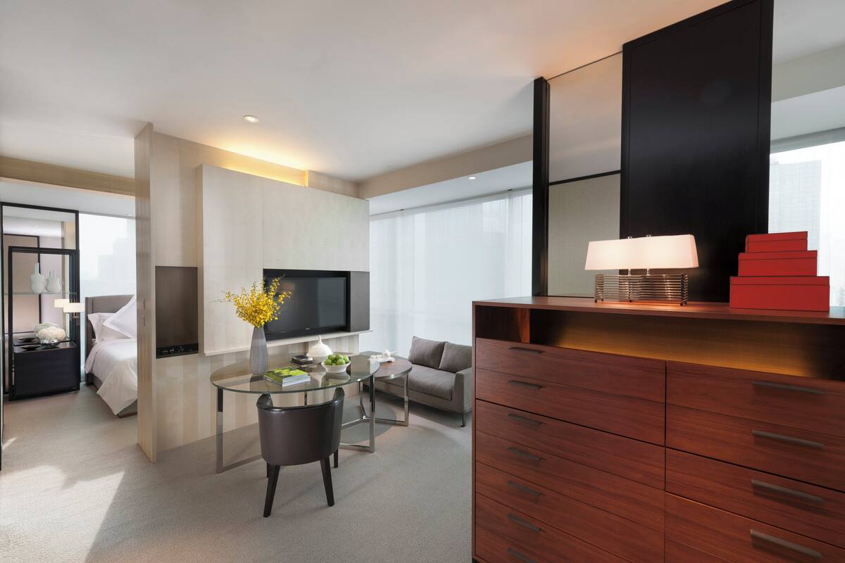 Une chambre d’hôtel moderne avec une table à manger en verre, un canapé, un téléviseur à écran plat et un meuble en bois.