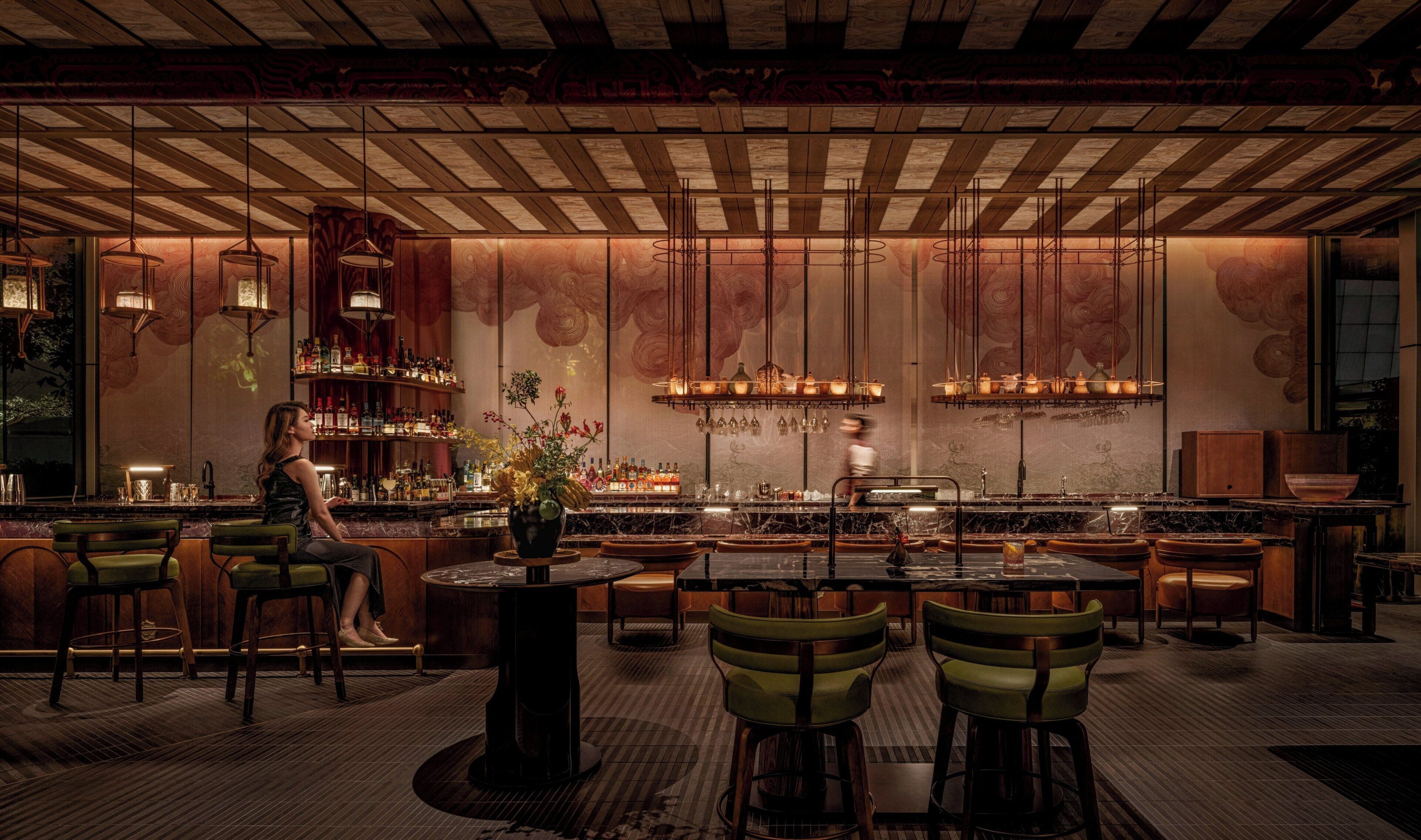 A bar area with wooden ceiling, green bar stools, and a person standing behind the bar.