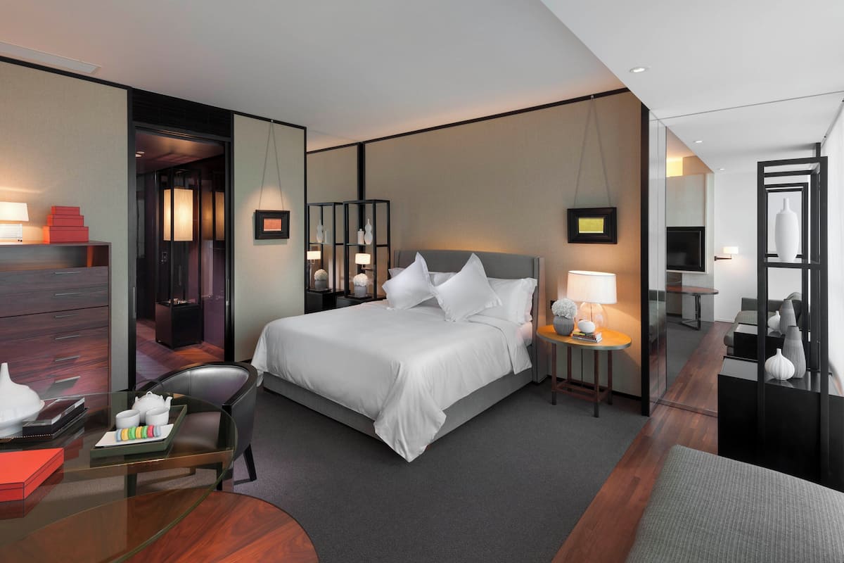 Une chambre d’hôtel moderne dotée d’un grand lit, de tables de chevet, d’un coin salon et d’une cloison en verre.