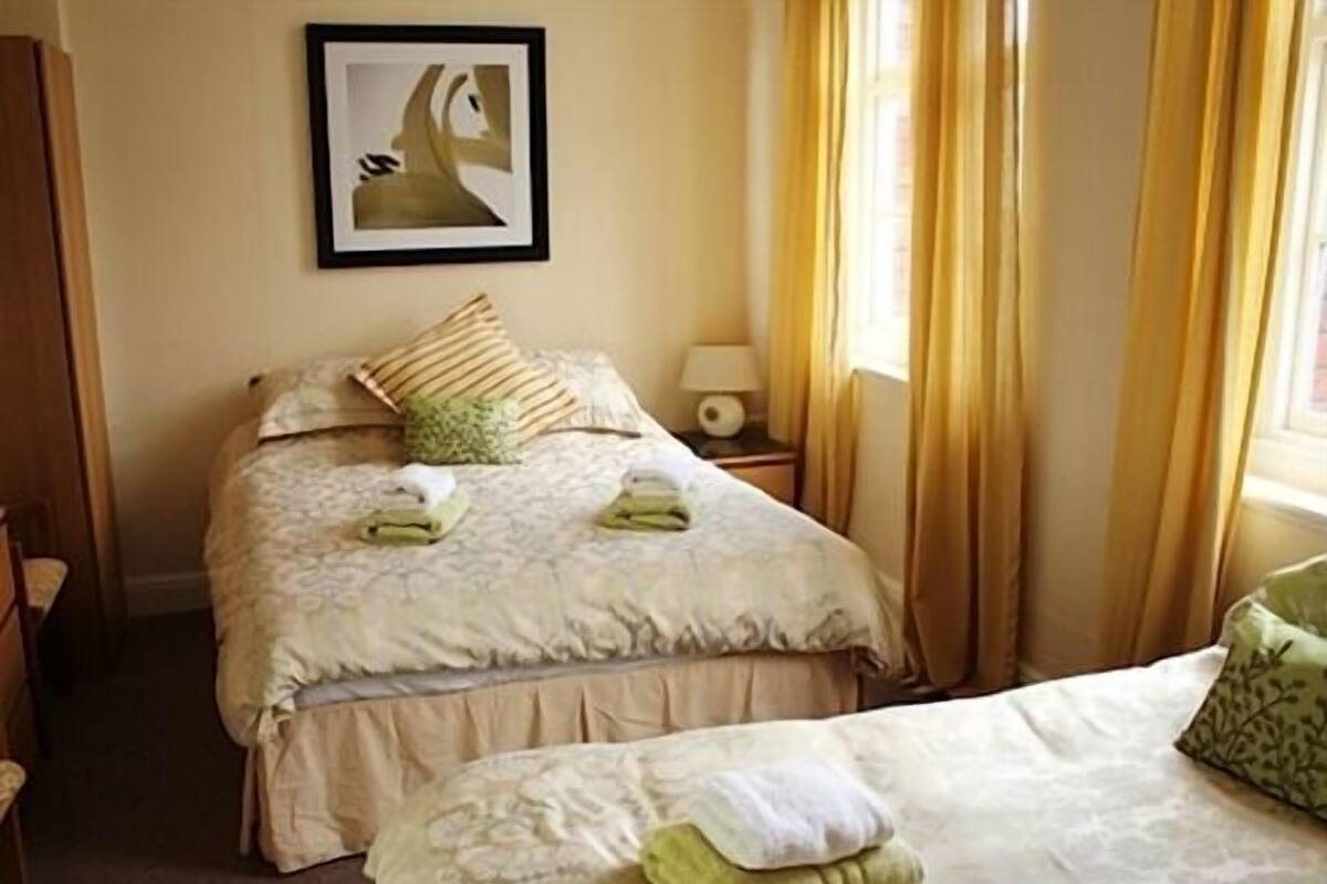 A hotel room with two beds, a bedside table with a lamp, and a framed picture on the wall.
