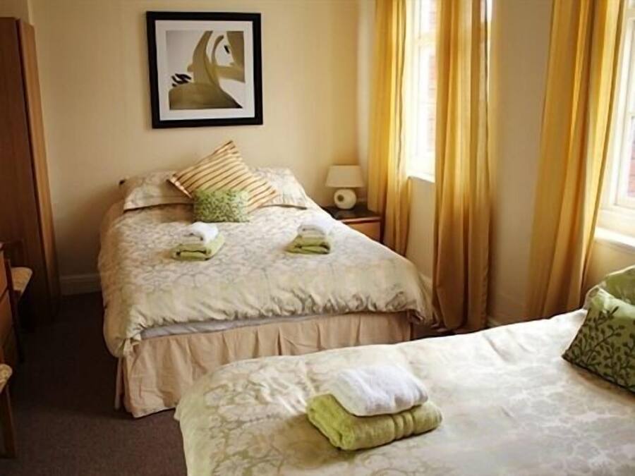 A hotel room with two beds, a bedside table with a lamp, and a framed picture on the wall.