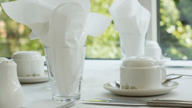 A table set with white tableware, including a glass, a cup, and a saucer, with a window view in the background. - The Liver View (Wallasey)