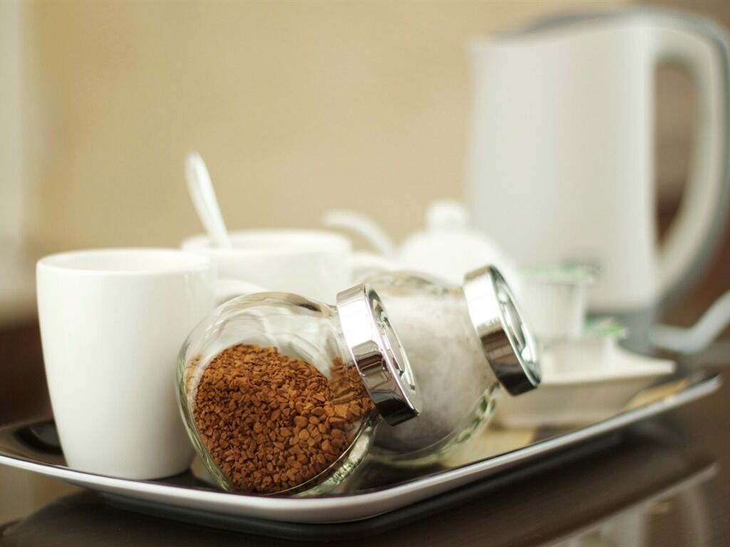 Una bandeja con un recipiente de vidrio con café, una taza blanca y una tetera blanca.