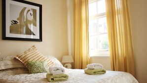 A neatly made bed with a floral-patterned bedspread, two pillows, and folded towels on the bed. - The Liver View (Wallasey)