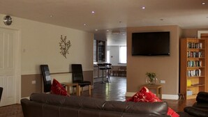 A living room with a brown leather sofa, two armchairs, a flat-screen TV, a bookshelf, and a dining area in the background. - The Liver View (Wallasey)