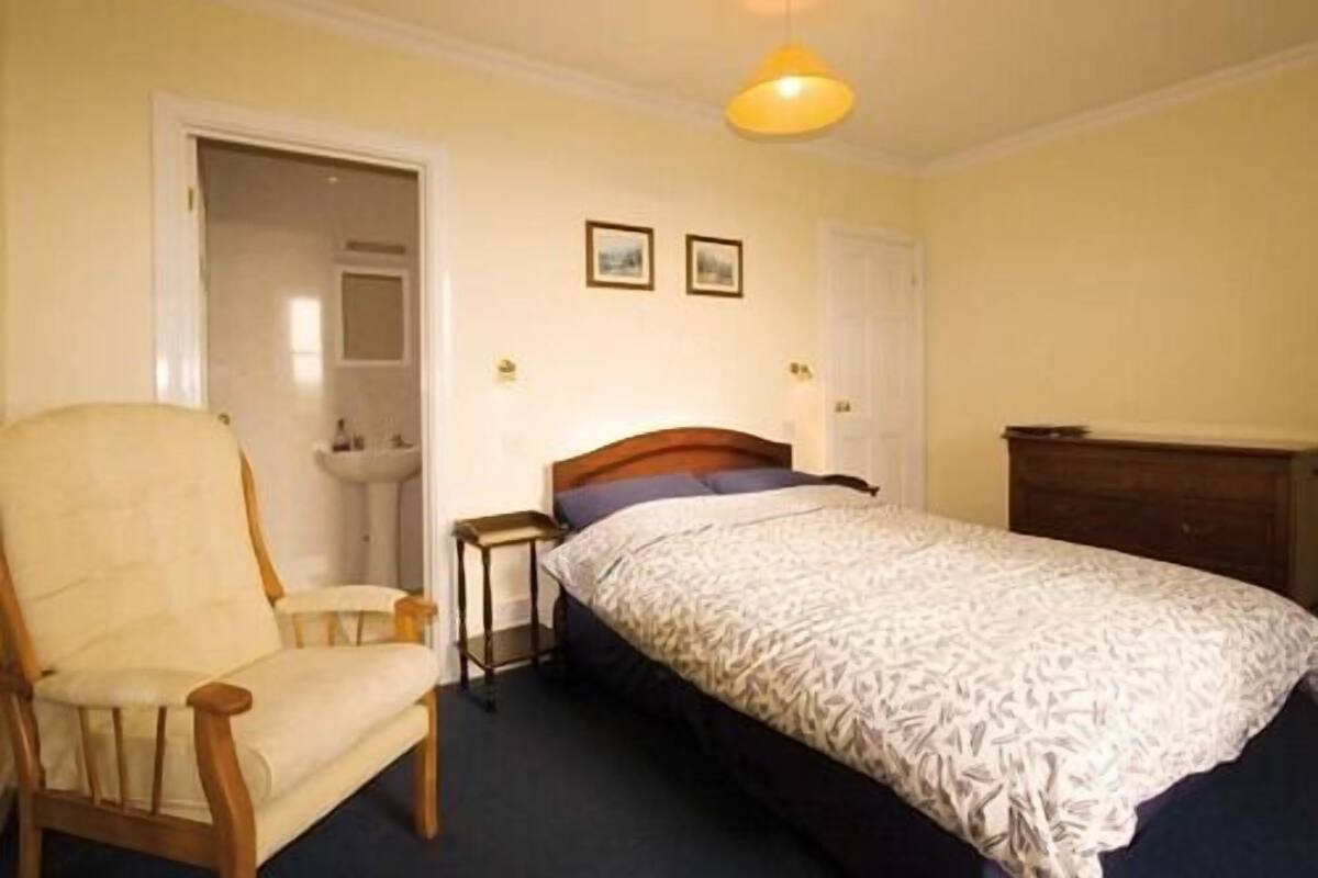 A bedroom with a bed, a chair, a bedside table, and a dresser.