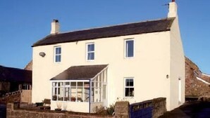 A two-story building with a white facade, a glass conservatory, and a stone wall. - East House (Chathill)
