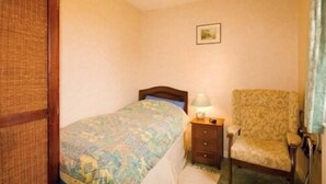 A bedroom with a bed, a nightstand, a chair, and a wall-mounted lamp. - East House (Chathill)