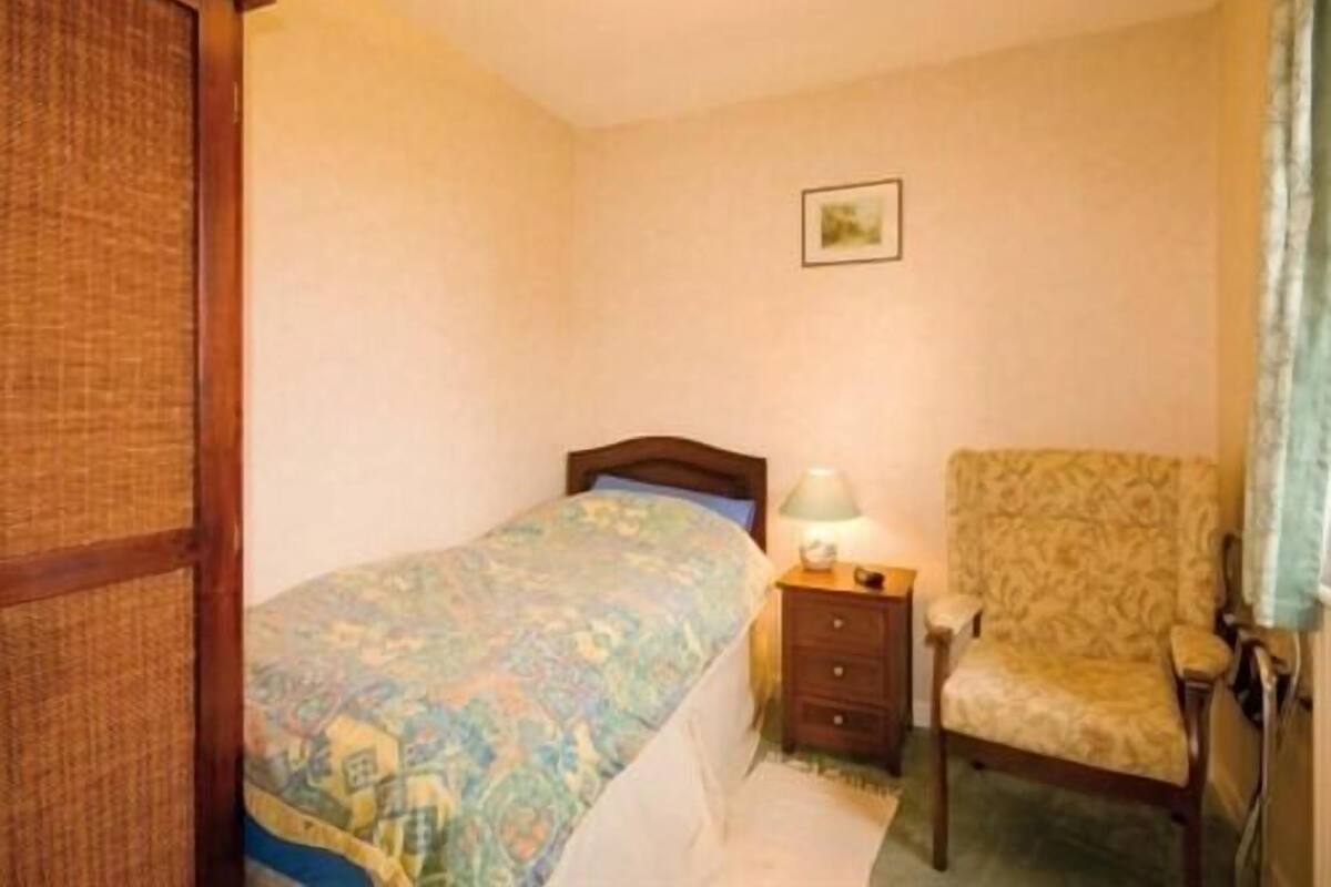 A bedroom with a bed, a nightstand, a chair, and a wall-mounted lamp.