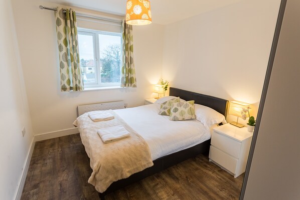 A bedroom with a bed, bedside tables, a window with curtains, a lamp, and a plant.