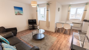 A living room with a sofa, a glass coffee table, a TV, and a dining area with chairs and a table. - Meridian Apartments - Southend (Southend-on-Sea)