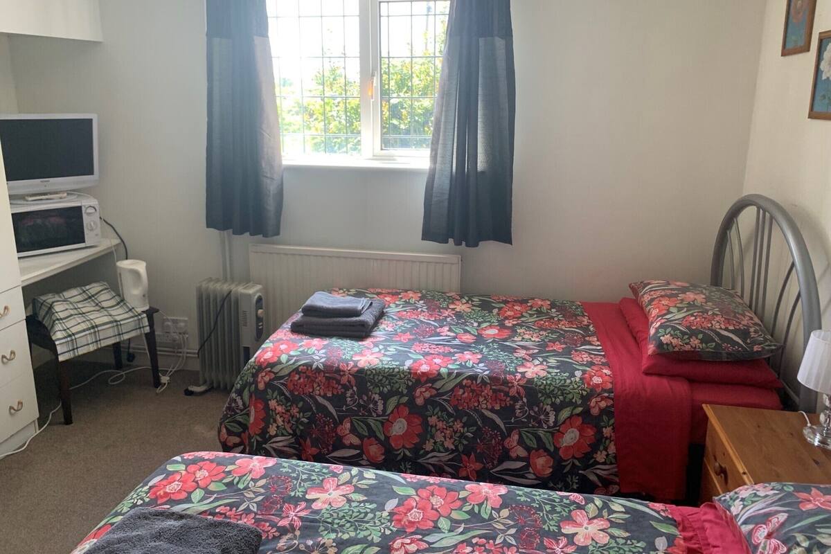 A bedroom with a bed, a desk with a computer, a radiator, and a window with curtains.