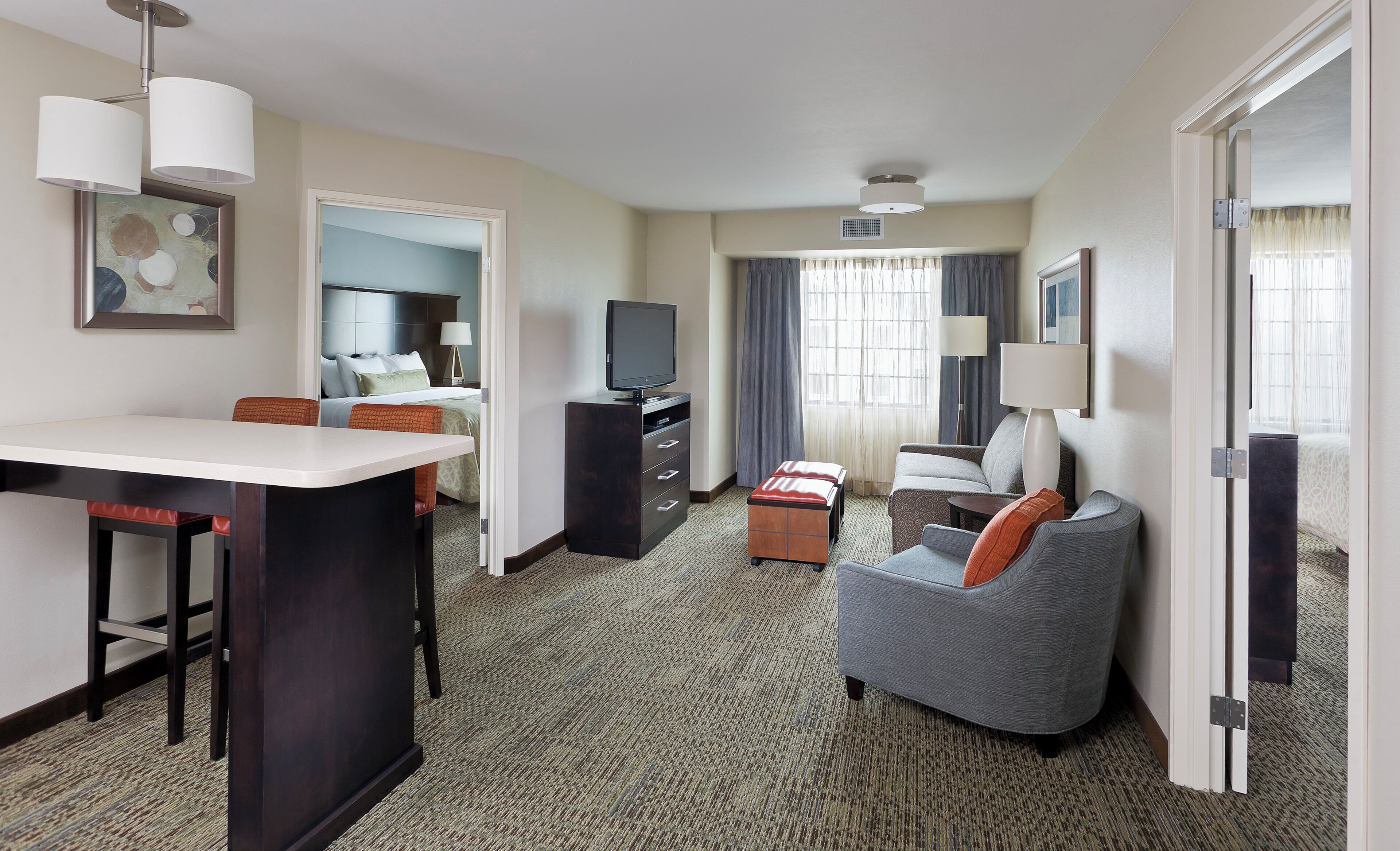 A hotel room with a dining area, a sofa, a TV, and a bed.