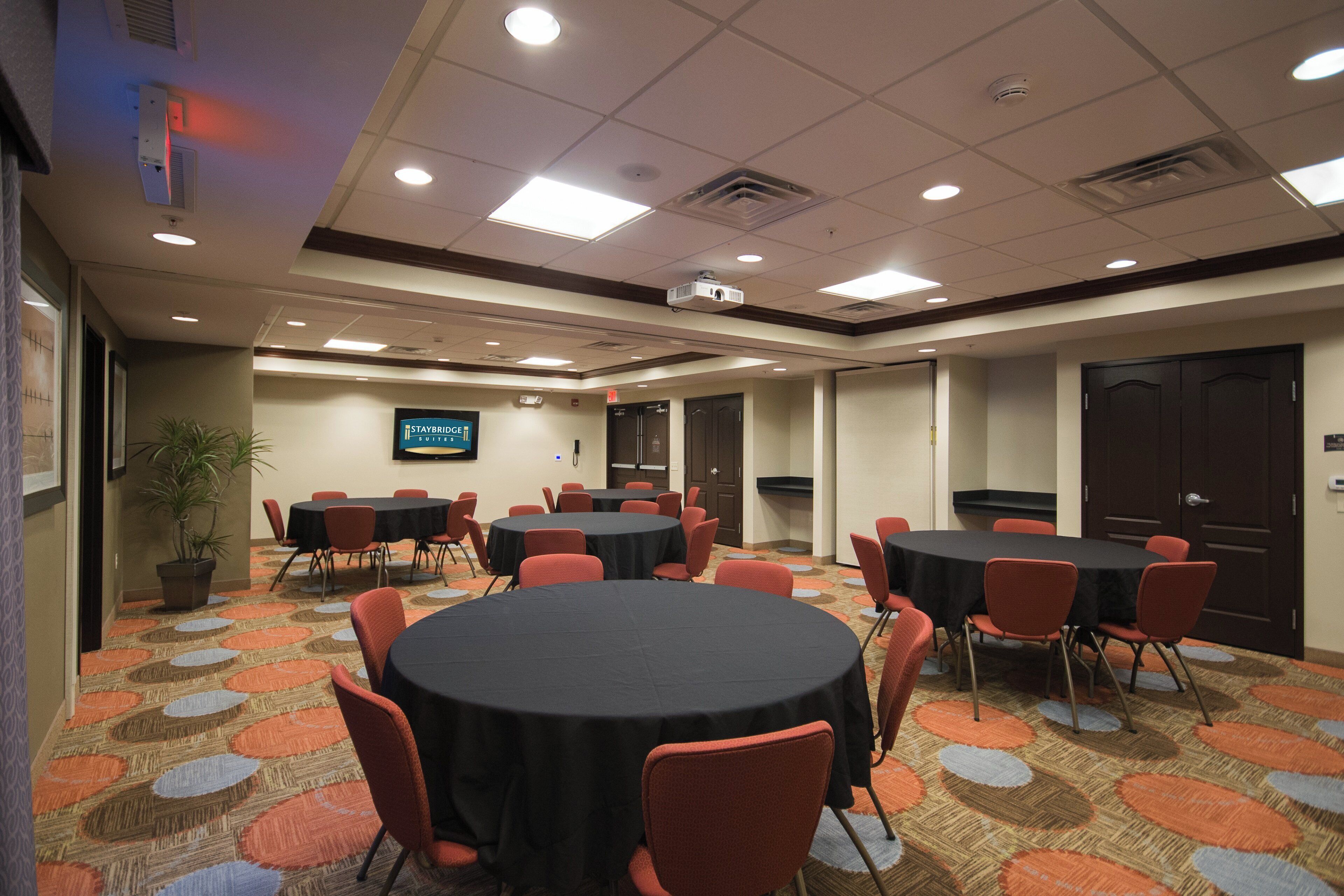 A conference room with multiple tables and chairs, a television screen, and a carpeted floor.