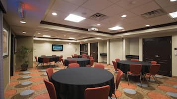 A conference room with multiple tables and chairs, a television screen, and a carpeted floor.