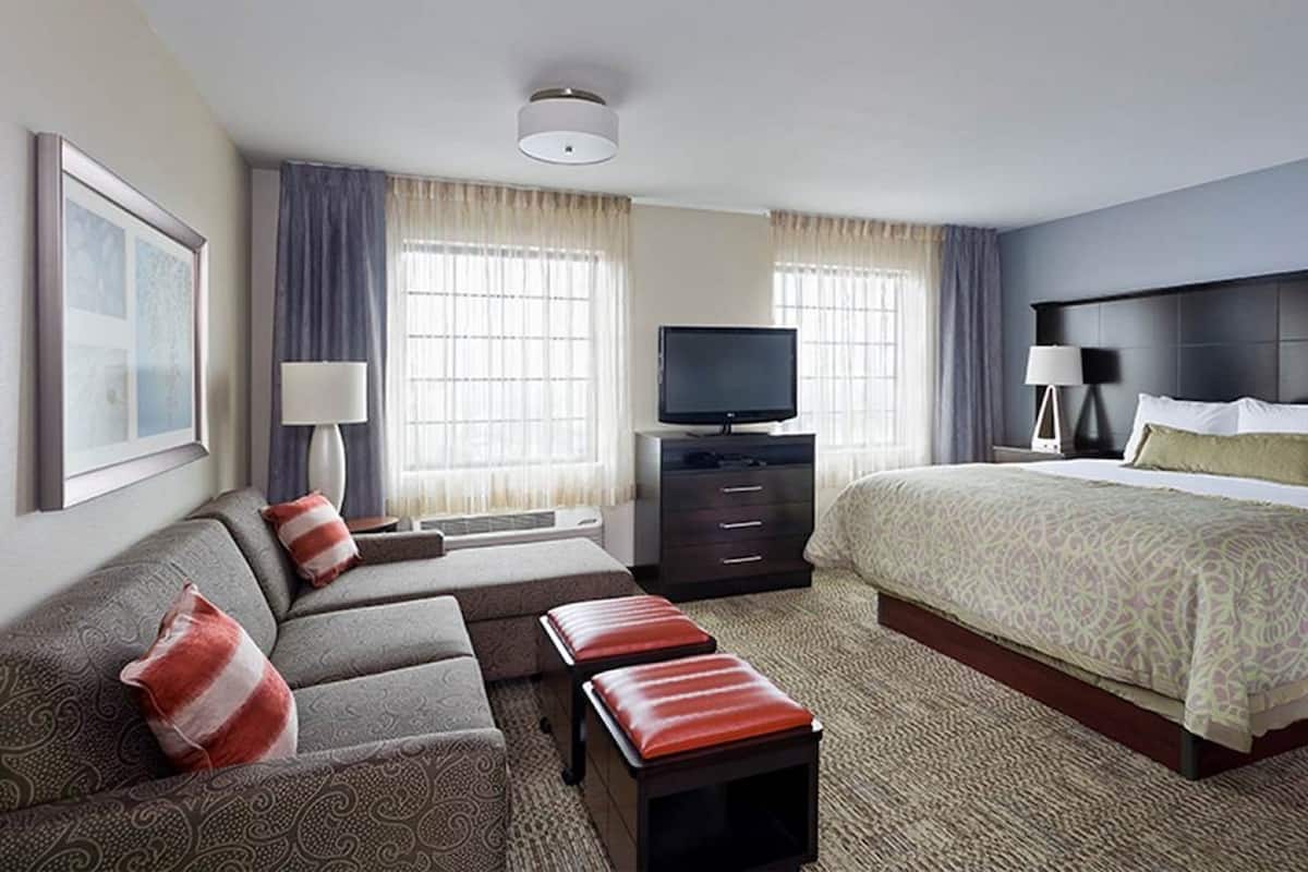 Habitación de hotel con cama, sofá, televisor y escritorio.