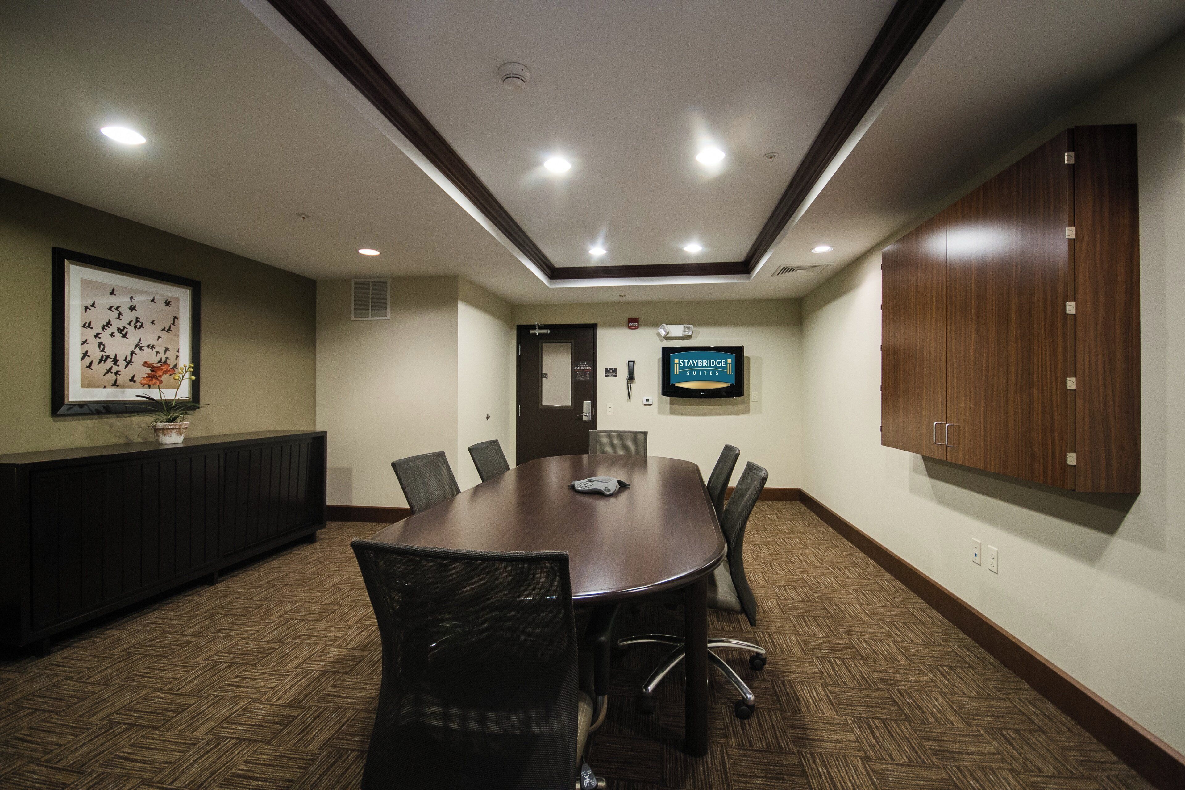 A conference room with a large table, chairs, a television, and a framed picture on the wall.