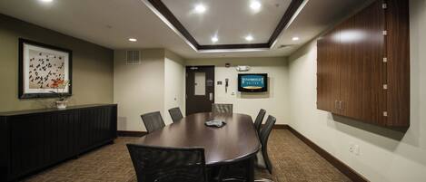 A conference room with a large table, chairs, a television, and a framed picture on the wall.
