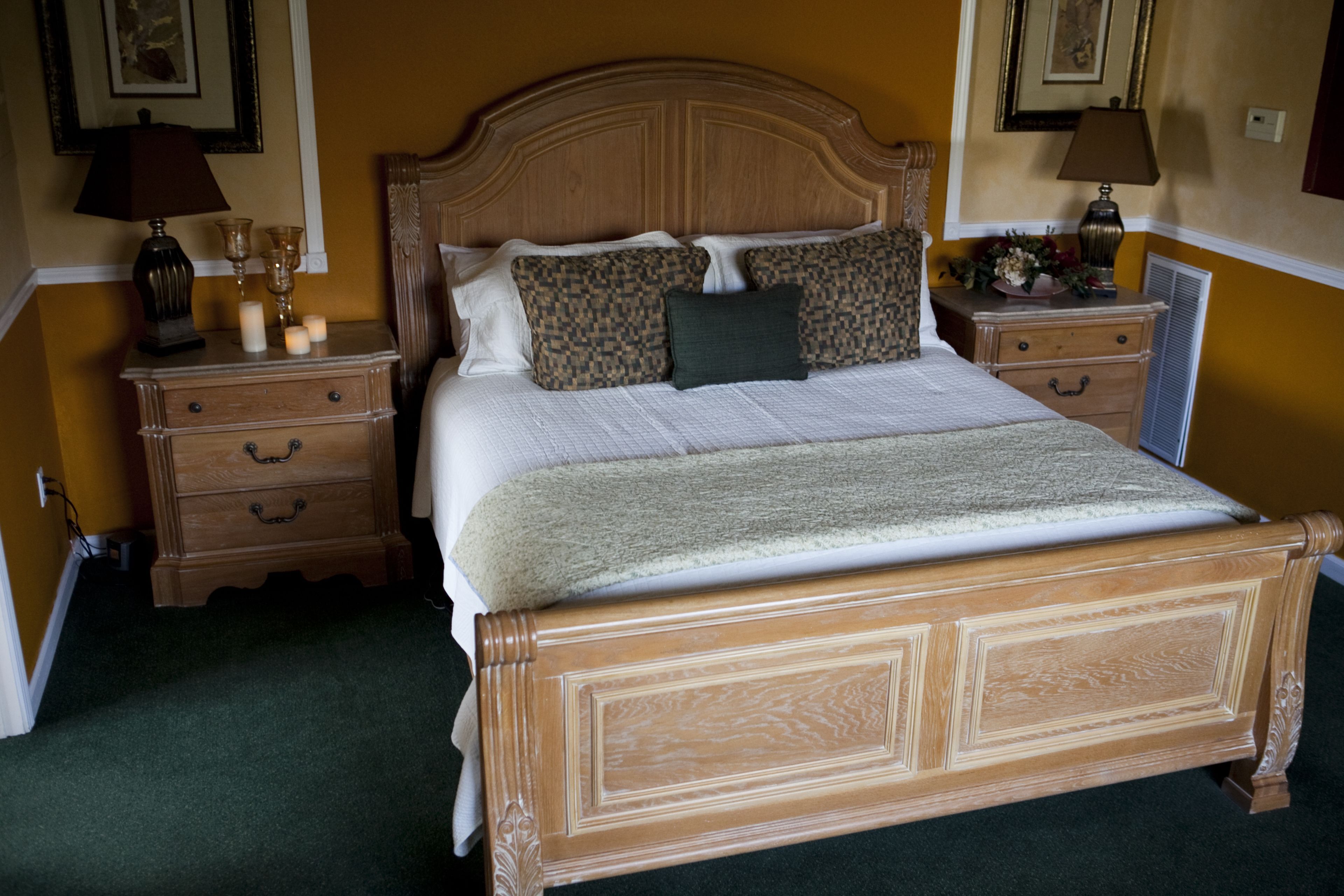 Una cama bien hecha con cabecera de madera, dos mesitas de noche con lámparas y un aparador.