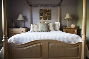 A four-poster bed with a quilted white bedspread, flanked by two bedside tables with lamps, a nightstand, and a wall-mounted artwork above. - The Purple Orchid Wine Country Resort & Spa (Livermore)