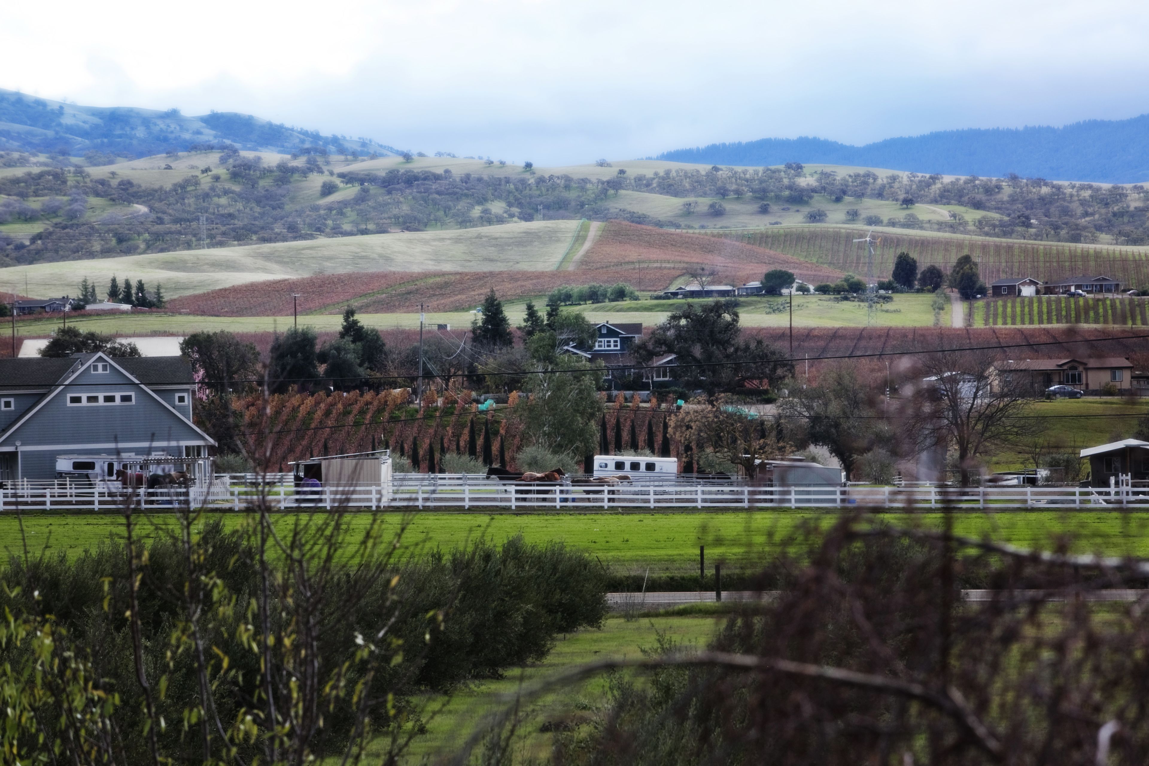 A rural landscape with a farmhouse, fields, and distant hills.