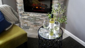 A cozy seating area with a stone fireplace, a small round table with wine bottles and glasses, and a comfortable armchair with a throw blanket. - The Purple Orchid Wine Country Resort & Spa (Livermore)