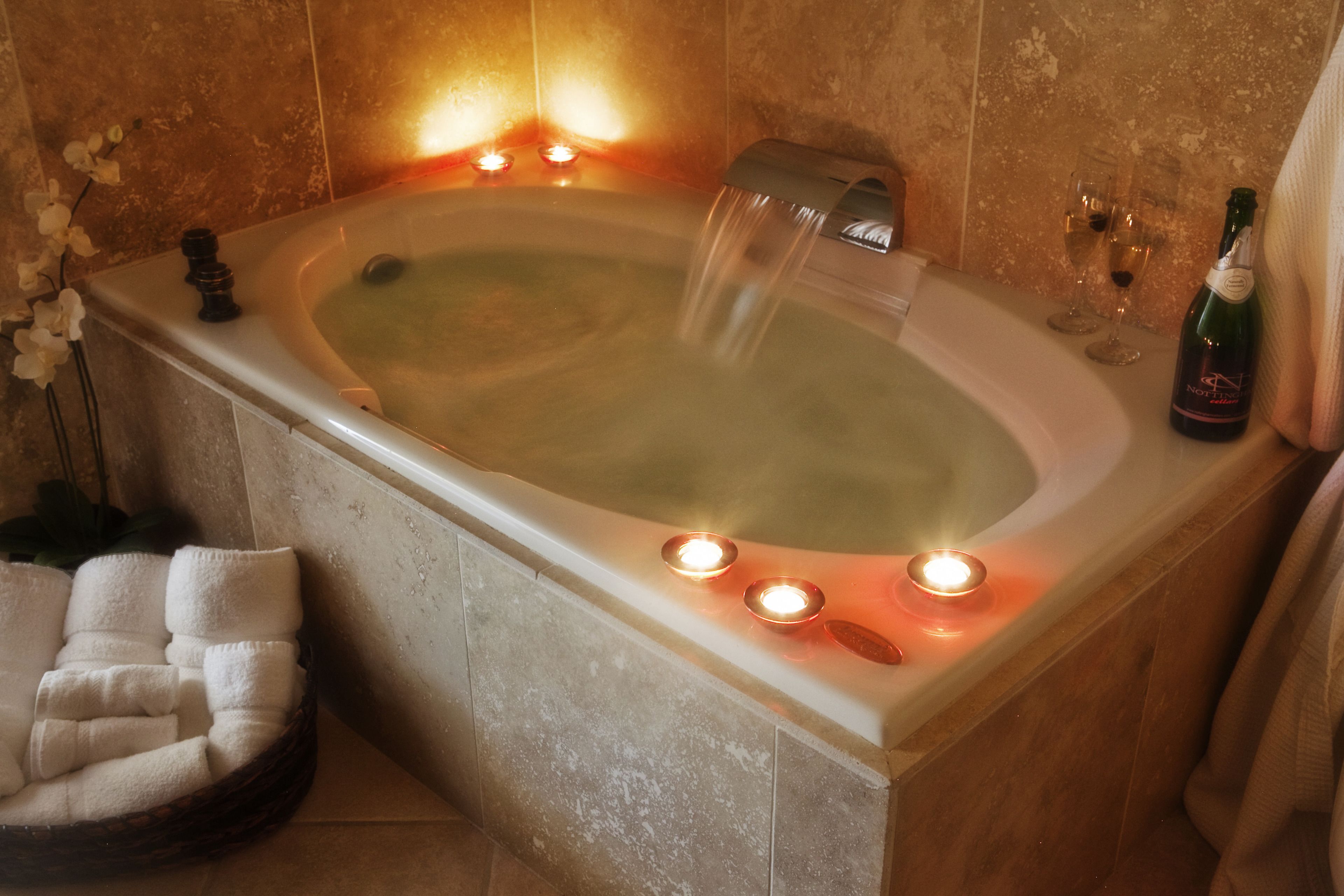 A bathtub with running water, candles, and a bottle of wine.