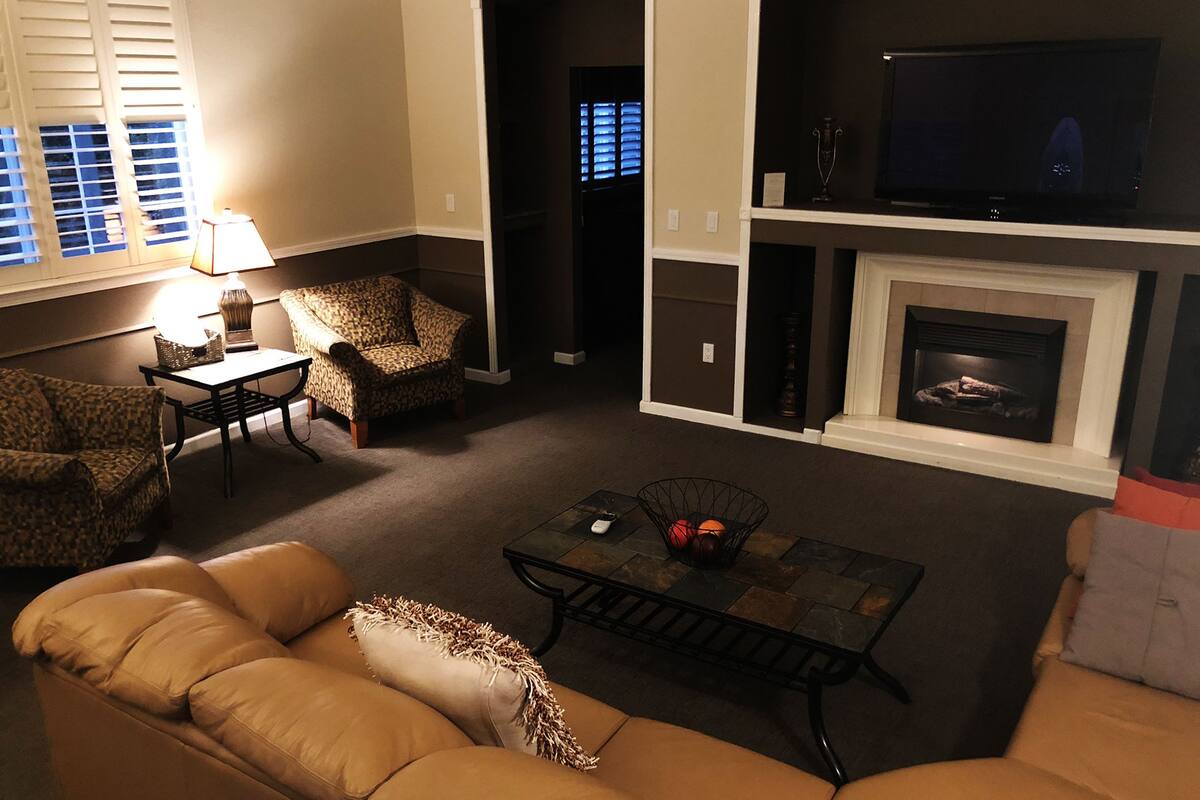 Una sala de estar con un sofá, dos sillones, una mesita de centro, un televisor y una chimenea.