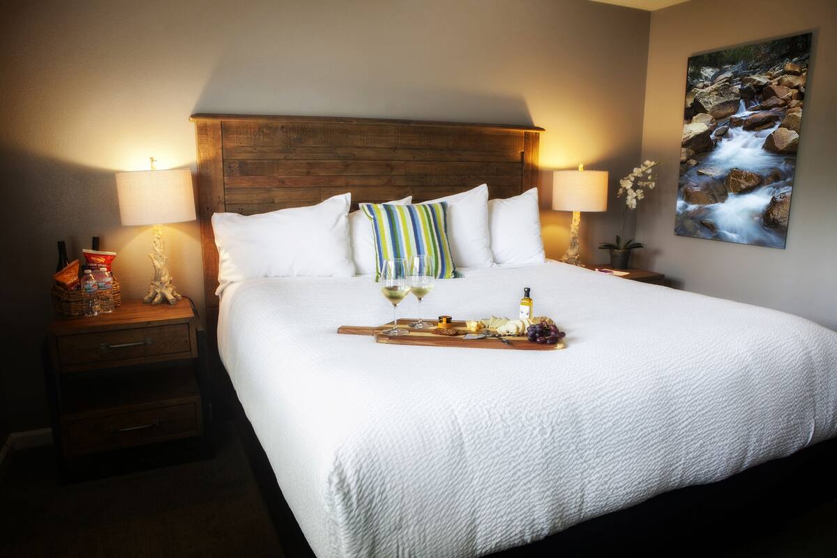 Una cama bien hecha con ropa de cama blanca, un cabecero de madera y una mesita de noche con una lámpara y una pequeña estatua.