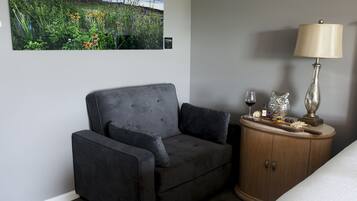 A room with a grey sofa, a wooden cabinet with a lamp, and a painting of a field.
