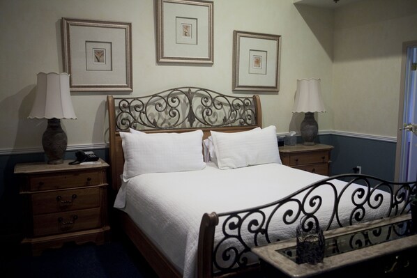 Una cama bien hecha con un tablero de cabecera decorativo, dos mesitas de noche con lámparas y cuadros enmarcados en la pared.
