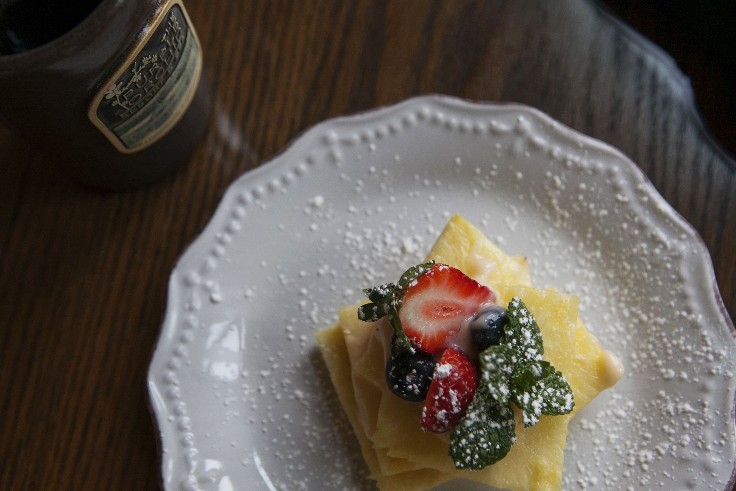Un dessert présenté sur une assiette, composé de fraises et de myrtilles, saupoudré de sucre glace, et posé sur une table en bois.