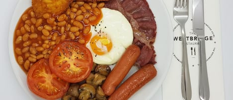 Un plato de comida para el desayuno con frijoles, huevos, tomates, champiñones, salchichas y tocino.
