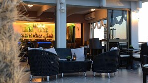 An outdoor seating area with wicker furniture, a bar in the background, and a view of the city. - Marianna Hotel (Kos)