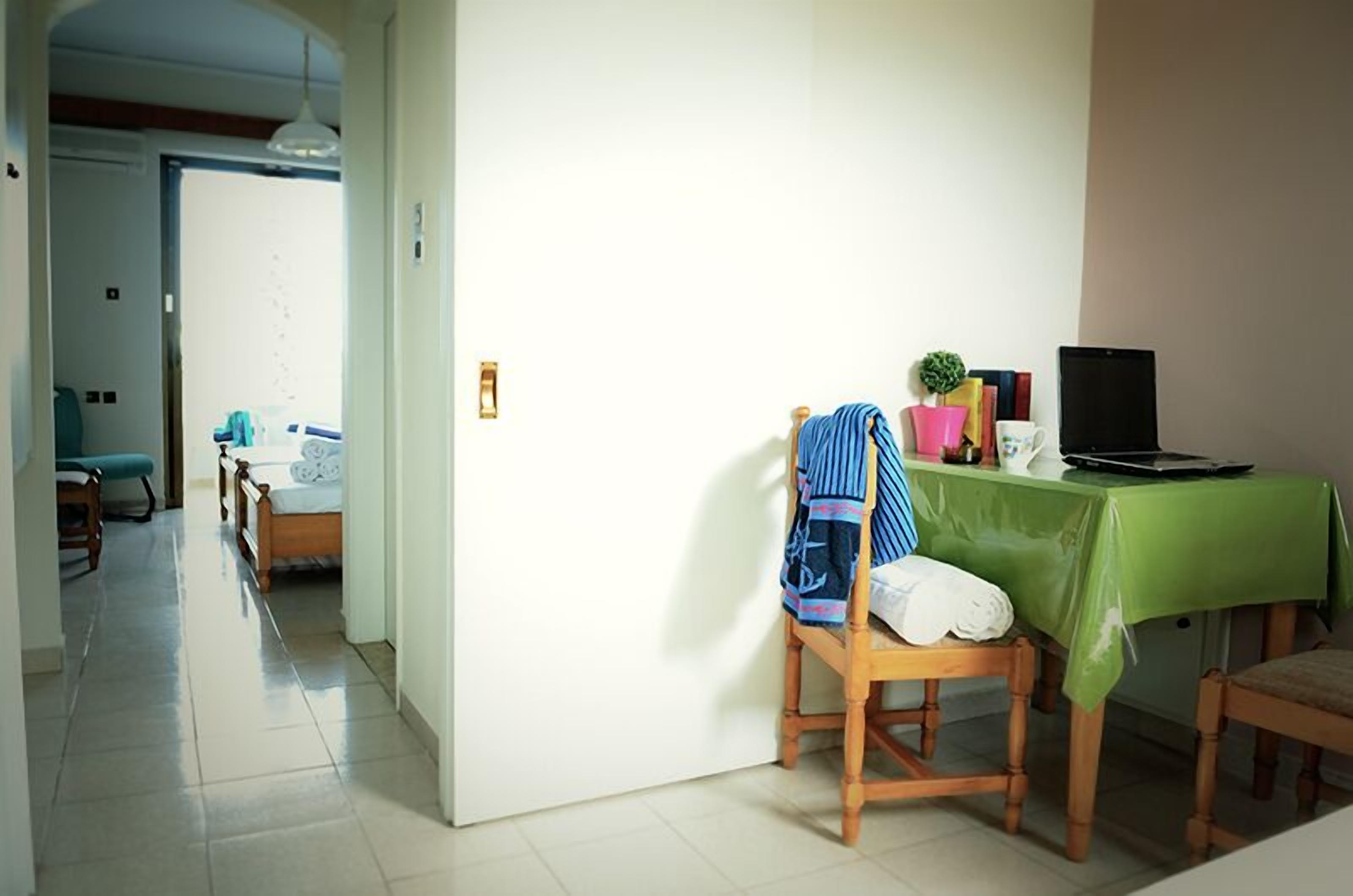 Una habitación con una cama, una silla, una mesa con una computadora portátil y un mantel verde.