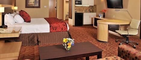 Een hotelkamer met een bed, een bureau, een stoel, een kitchenette en een televisie.
