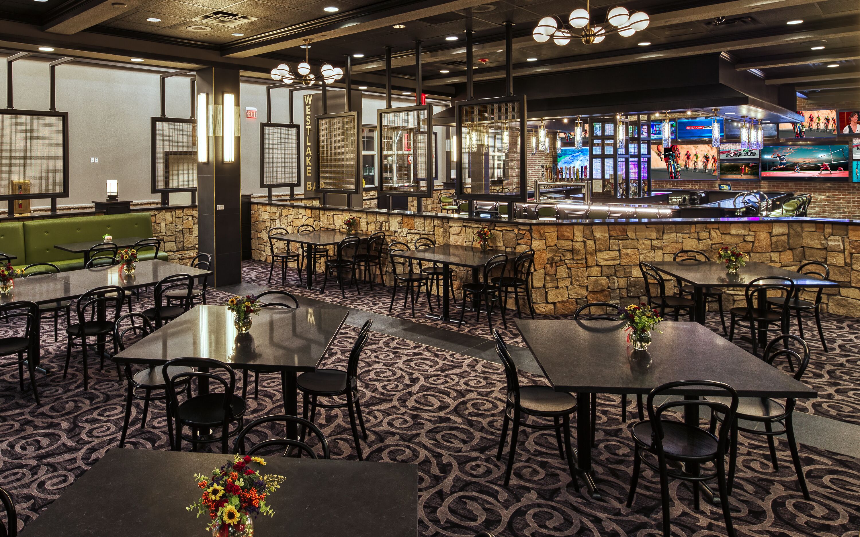 A restaurant with multiple tables and chairs, a stone wall bar area, and a television screen displaying sports.