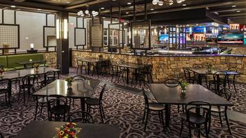 A restaurant with multiple tables and chairs, a stone wall bar area, and a television screen displaying sports.